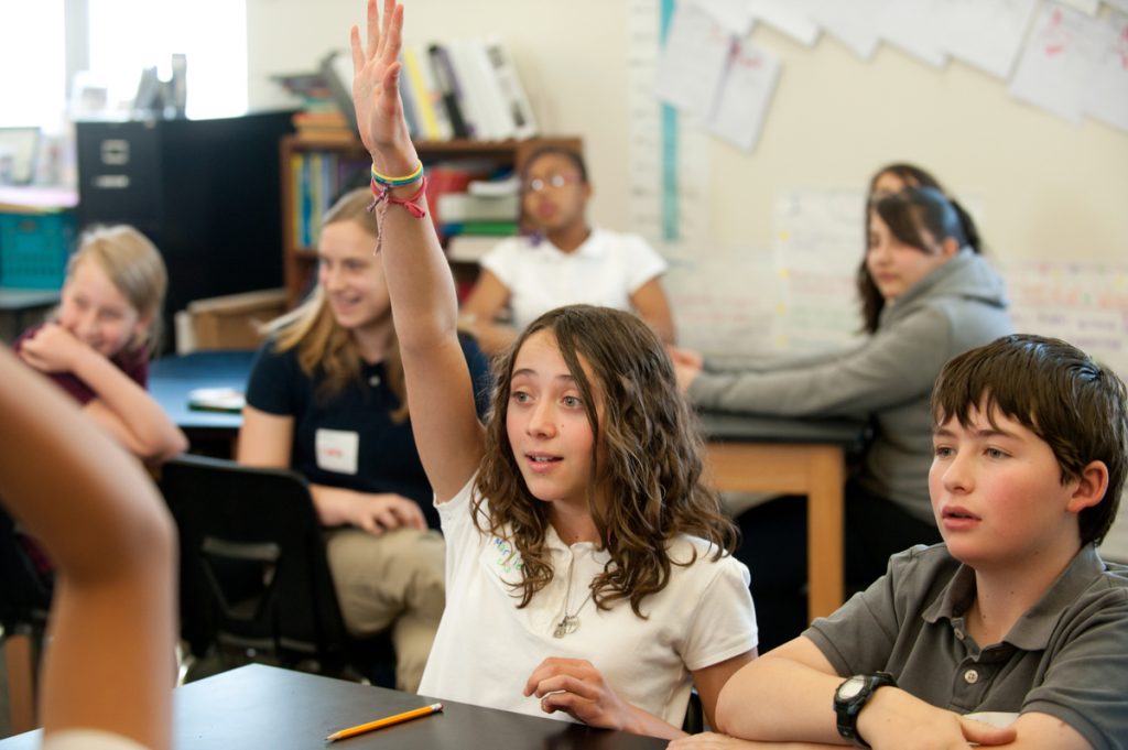 Junior Achievement girl raising her hand in classroom with Blue Federal Credit Union.