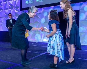 Judith Wagner shaking hands with 2 JA students on stage at the 2020 Colorado Business Hall of Fame.