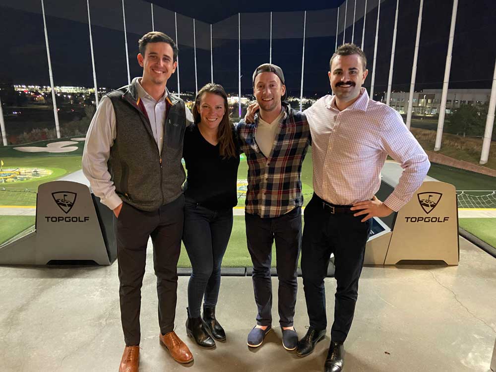 Four individuals standing in front of green at Top Golf